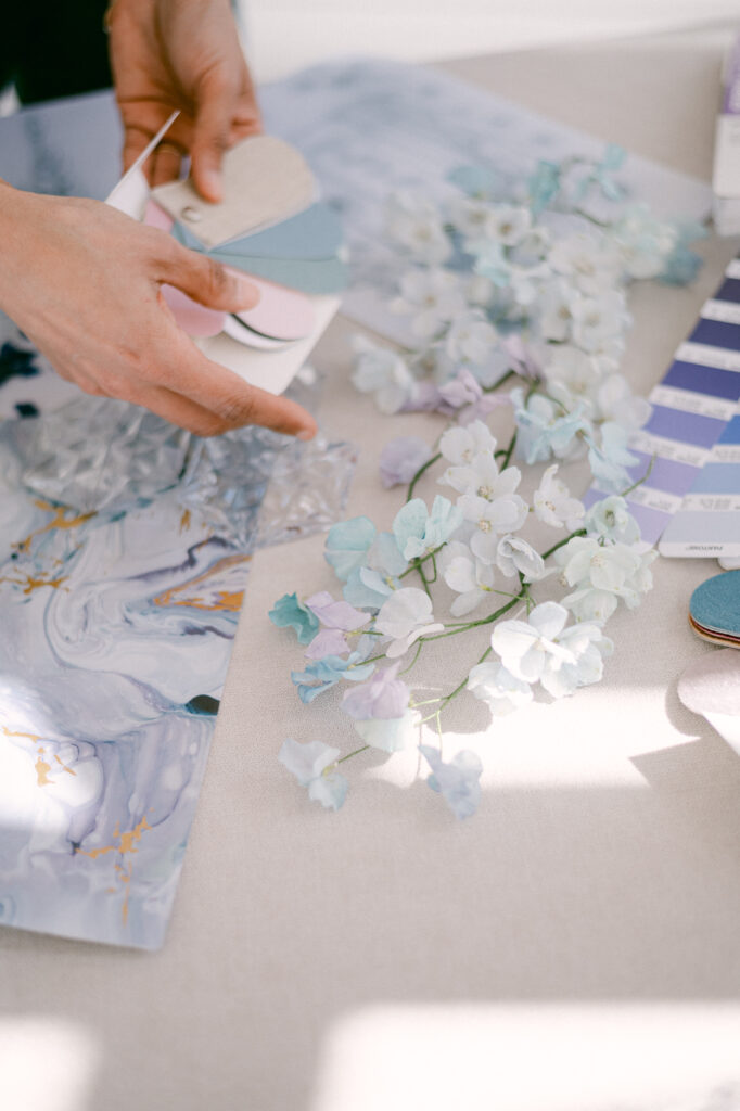 Feminine hand exploring palettes of materials and colours among airy flowers and marbled textures — a suspended moment of sensitive creation — Maison Bouchra.