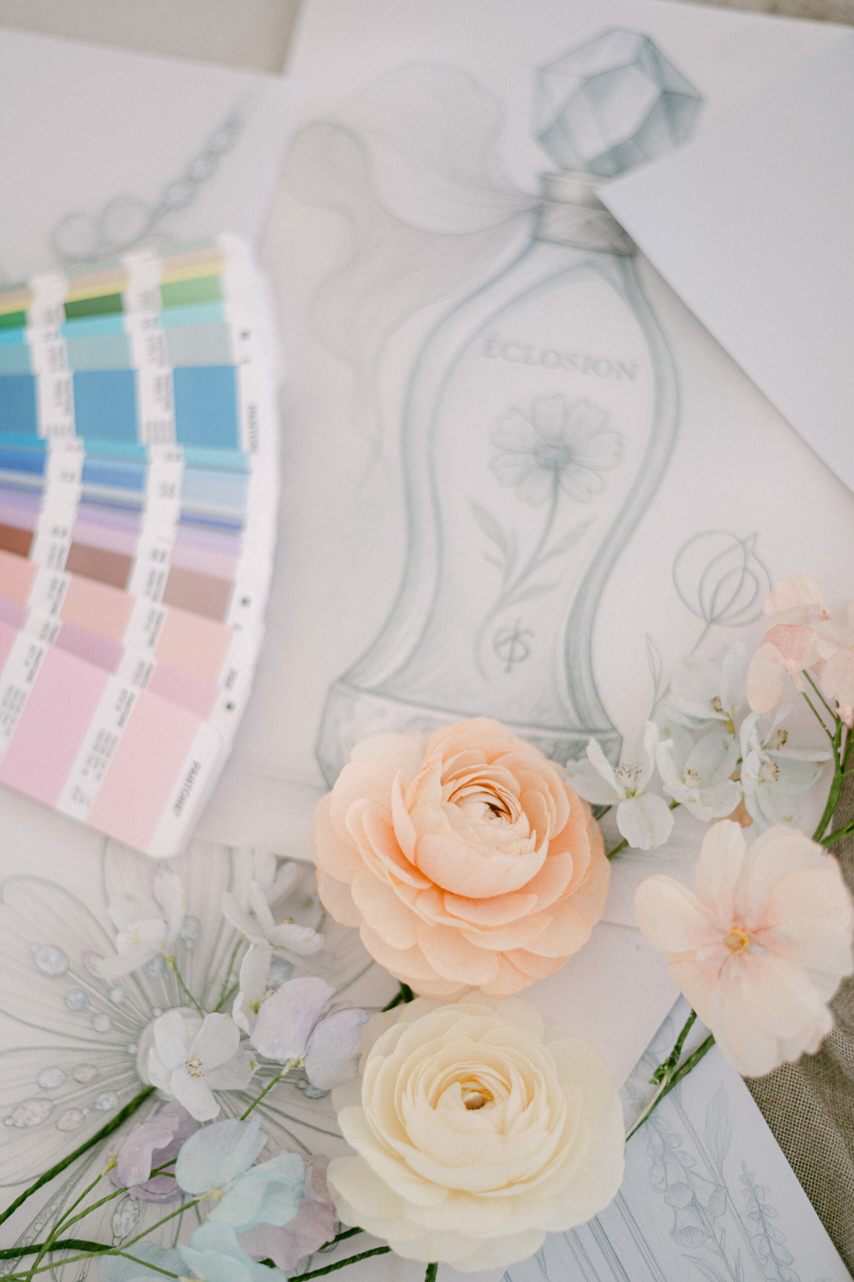 Ébauche de flacon poétique entourée de fleurs pastel et d’un nuancier, symbole d’un processus créatif sensoriel et raffiné – Maison Bouchra.